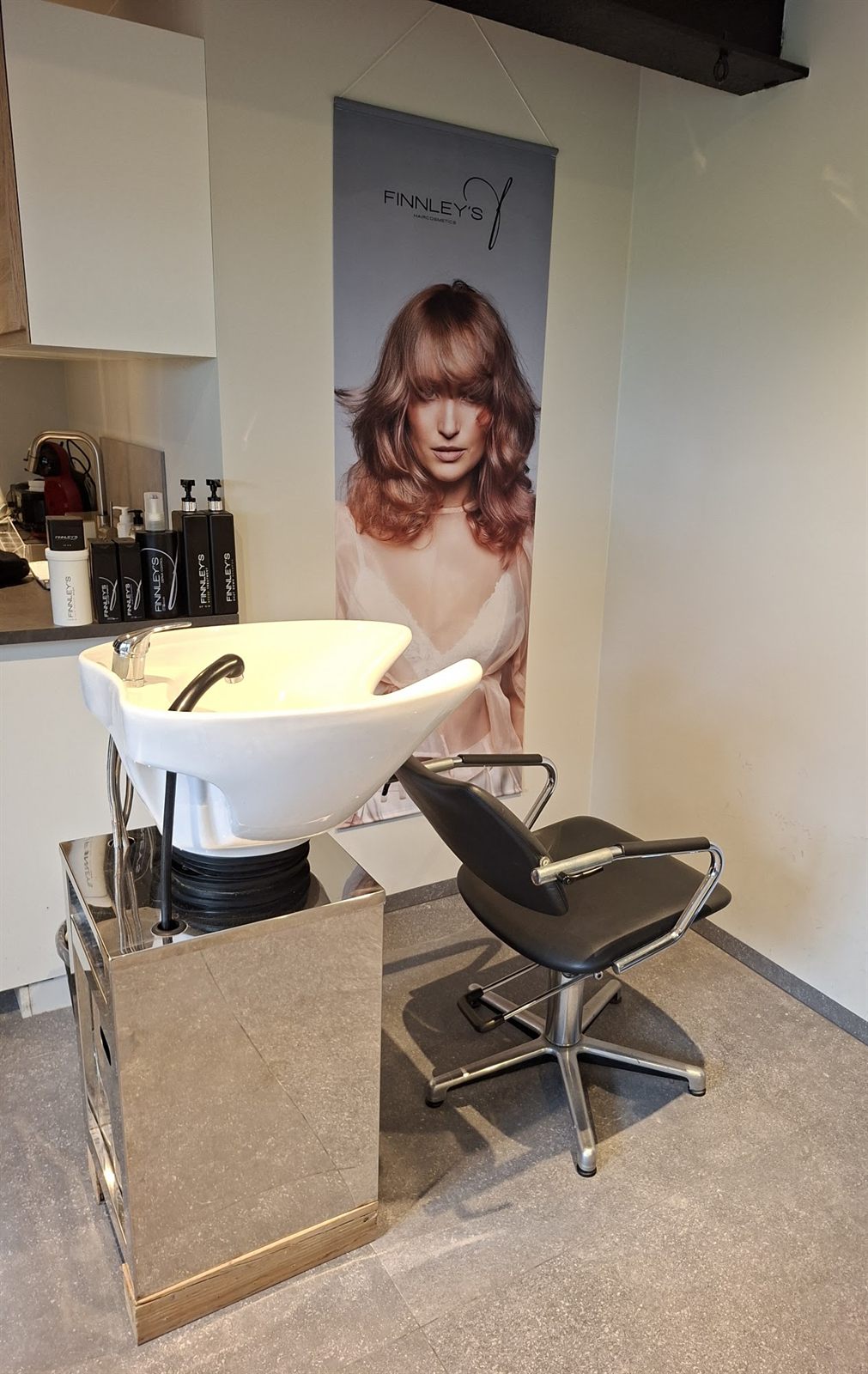 De salon: een wasbak, een kappersstoel en een poster van Finnley’s aan de muur